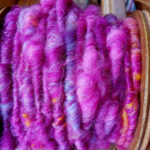 Close up view of a bobbin of corespun bright pink and purple yarn with pops of bright orange.