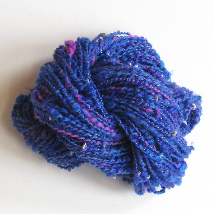 A skein of hand spun merino and recylced sari silk in rich blue with pops of bright pink, plied with a silver metallic thread and silver metal beads.