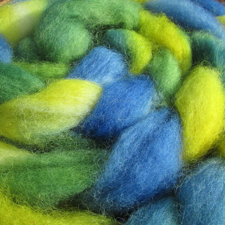 Close up view of a braid of hand dyed fibre in blue, green and yellow.