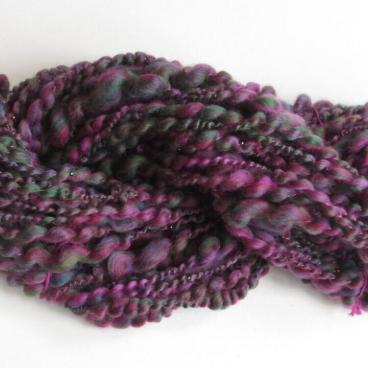 Close up view of a skein of hand spun yarn in heathery purples and greens with beads.