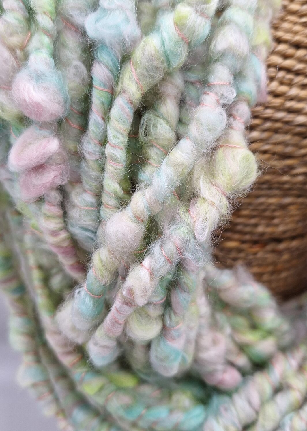 Close up of hand spun merino and silk cowl neck warmer in pastel shades of green, pink, blue and white on a rattan bust