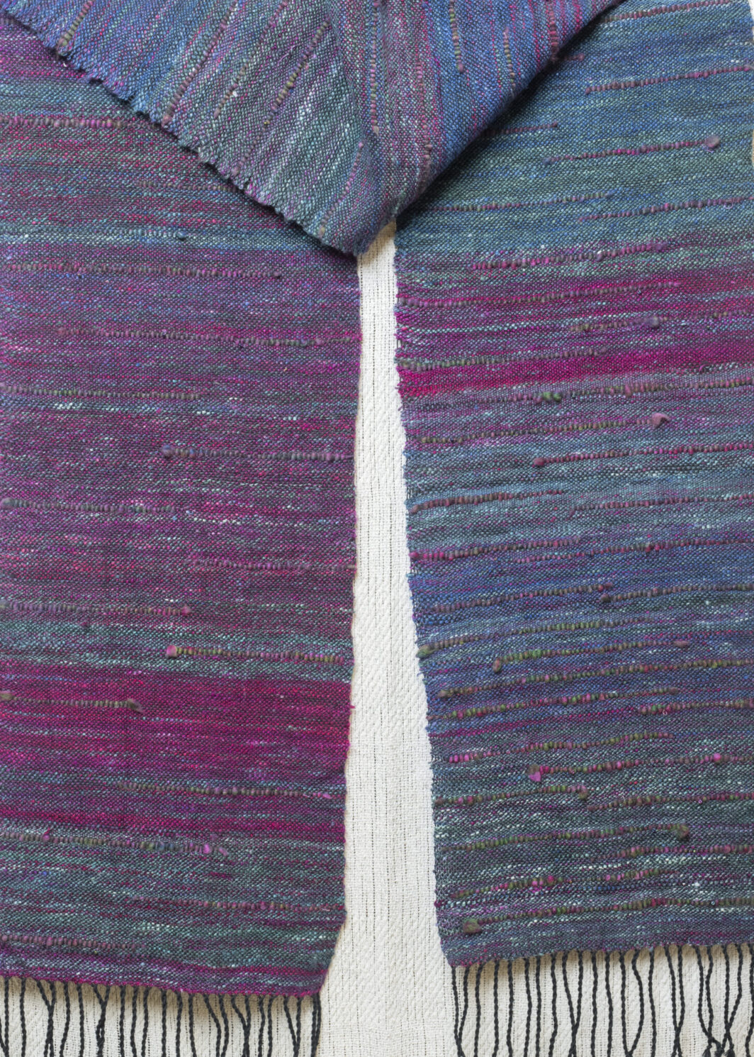A beautiful silk scarf in oil slick colours of teals, blues and deep pinks is draped and hanging down.