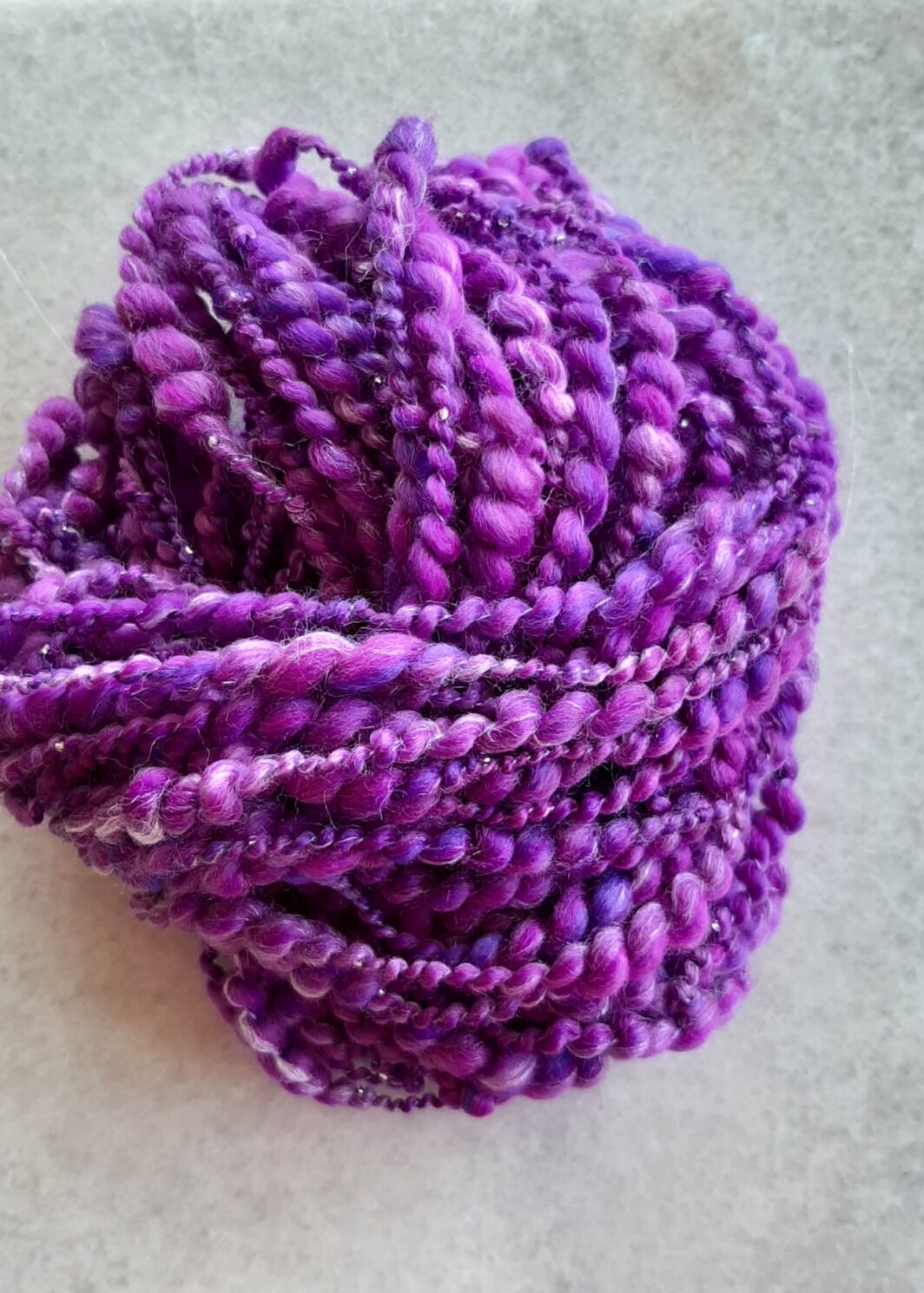 Purple and lilac hand spun merino and silk hand spun thick and thin beaded yarn arranged on a grey marble background