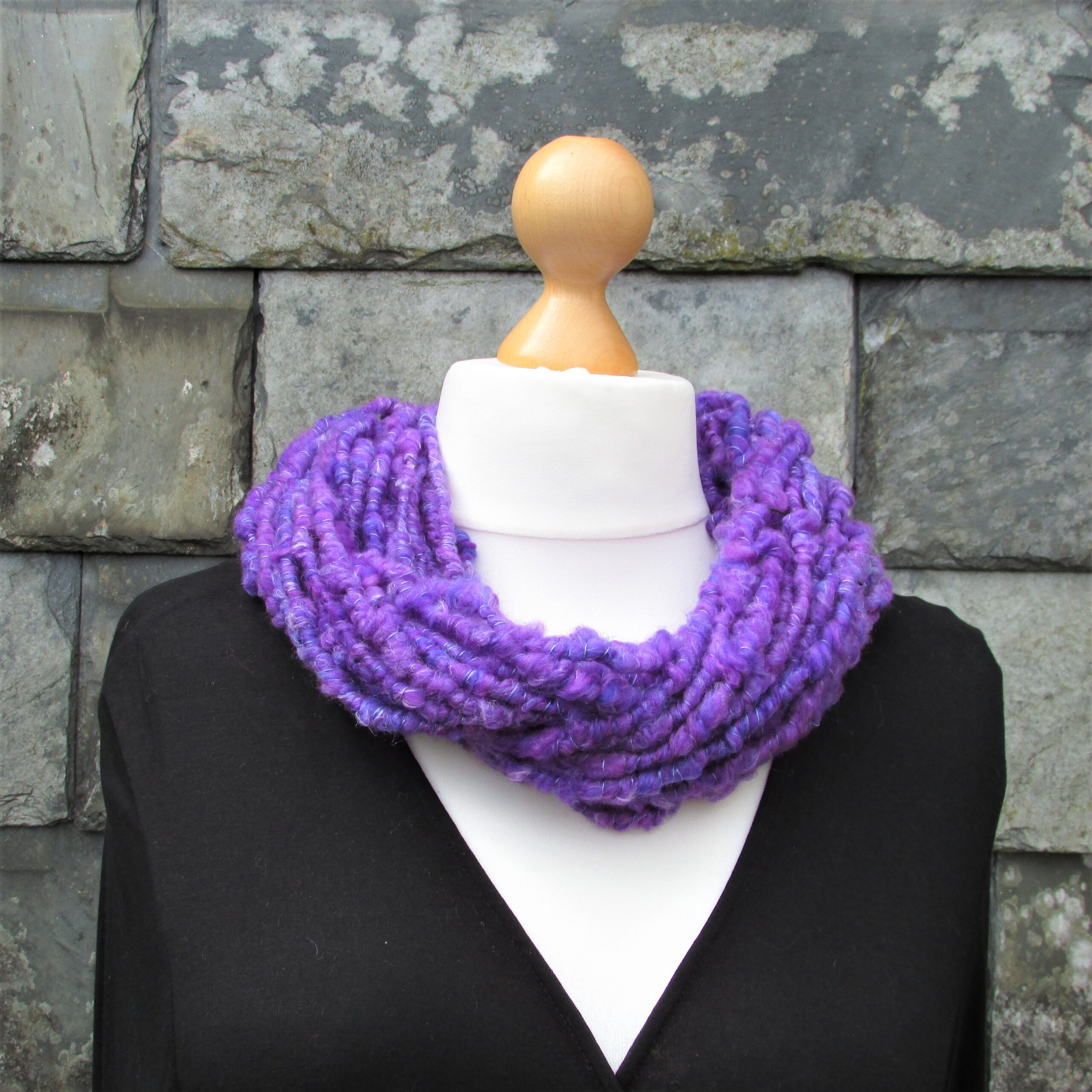 Tailor's dummy is modelling a bluey purple hand spun yarn cowl in front of a slate hung wall.