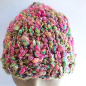 Close up of a hand knitted beanie hat on a mannequin. The hat has been knitted with handspun merino and silk thick and thin yarn in bright yellow, pink, turquoise and lime green with tiny pink glass beads.