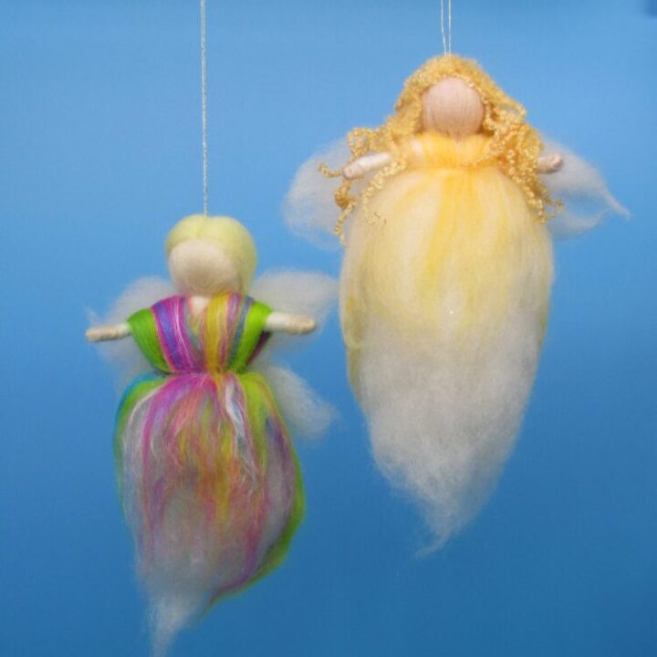 Two needle felt fairies, one golden and white and the other in green, pink and yellow, suspended with golden thread before a sky blue background.