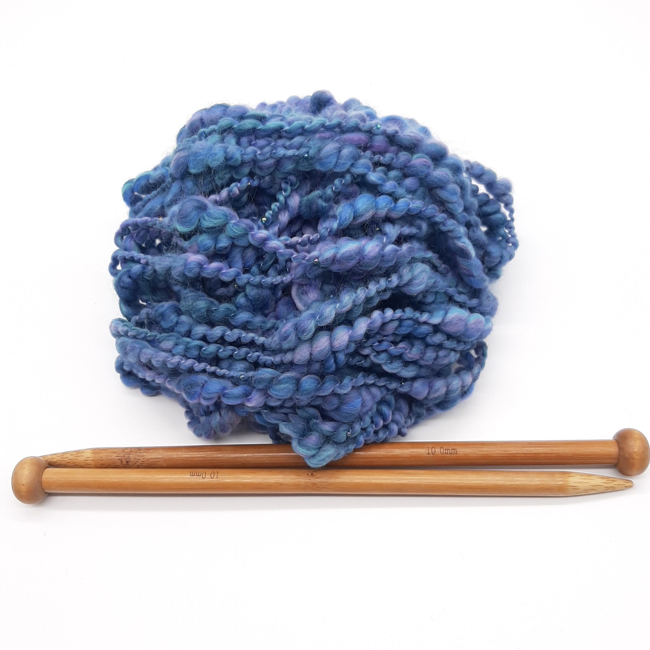 A ball of Daymer Storm handspun beaded merino yarn in blues with a hint of lilac, above a pair of bamboo knitting needles.
