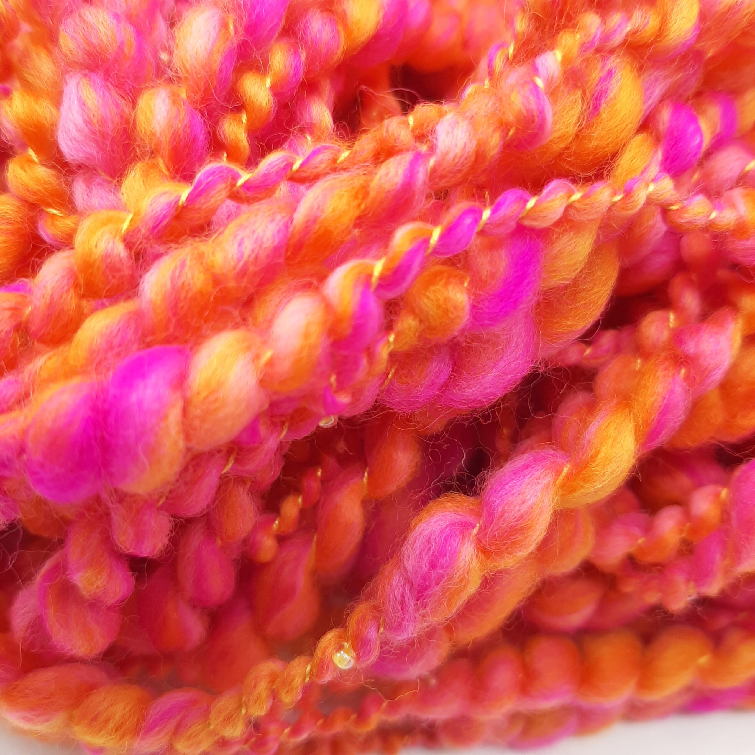 A close up view of Fruit Salads hand spun merino beaded yarn in vibrant shades of orange and pink.