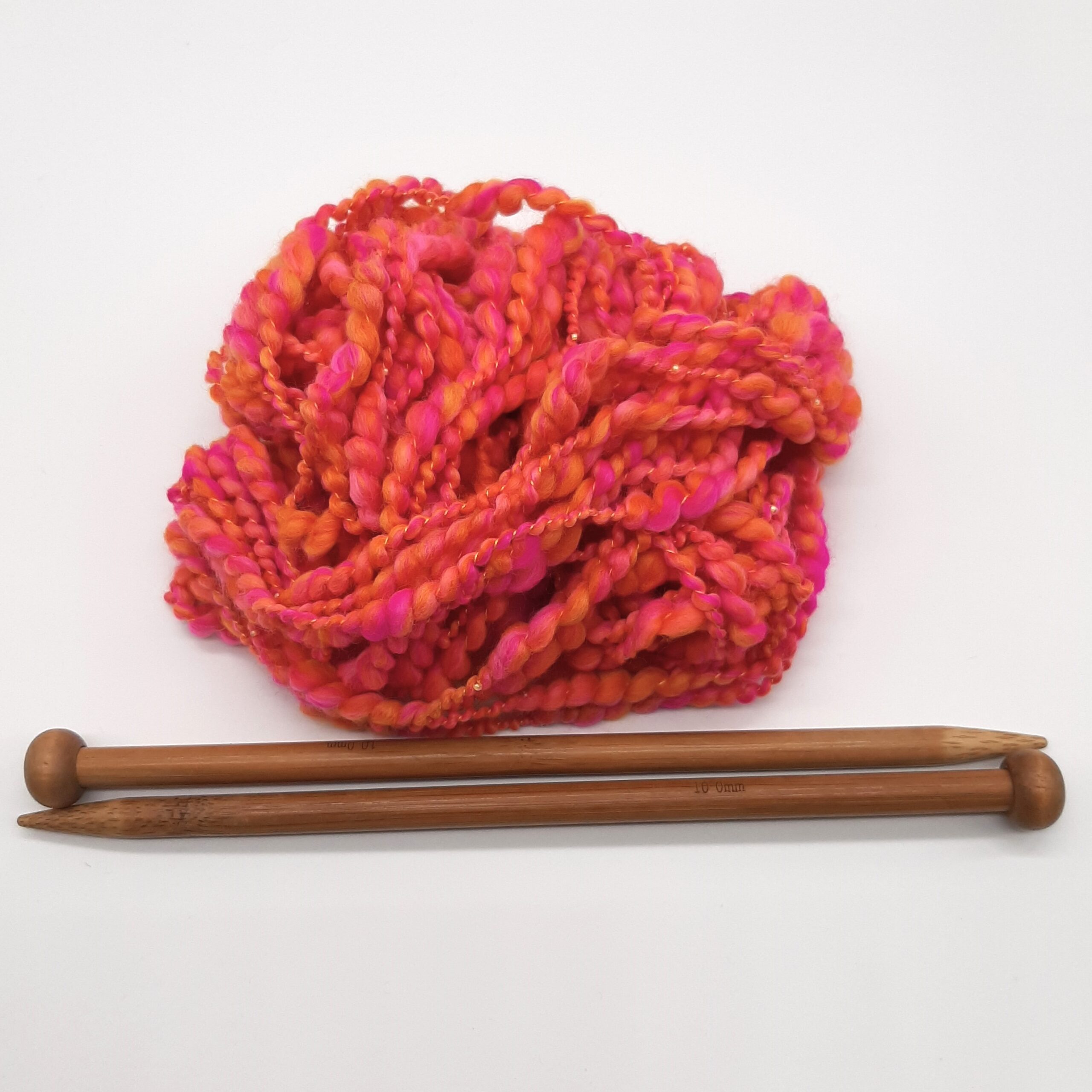 A ball of Fruit Salads hand spun merino beaded yarn in vibrant shades of orange and pink, above a pair of bamboo knitting needles.