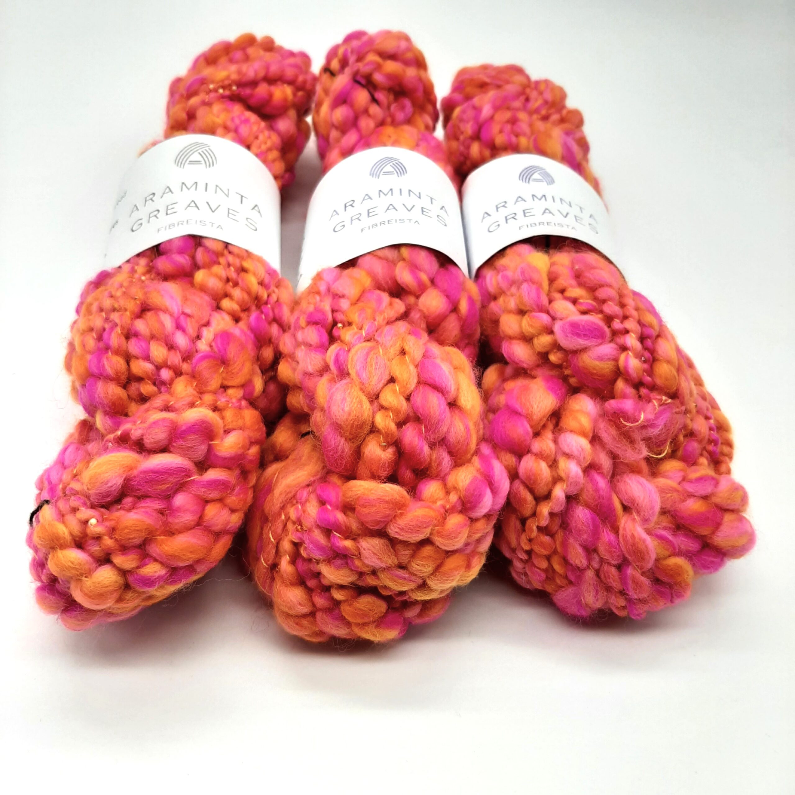 Three skeins of Fruit Salads hand spun merino beaded yarn in vibrant shades of orange and pink