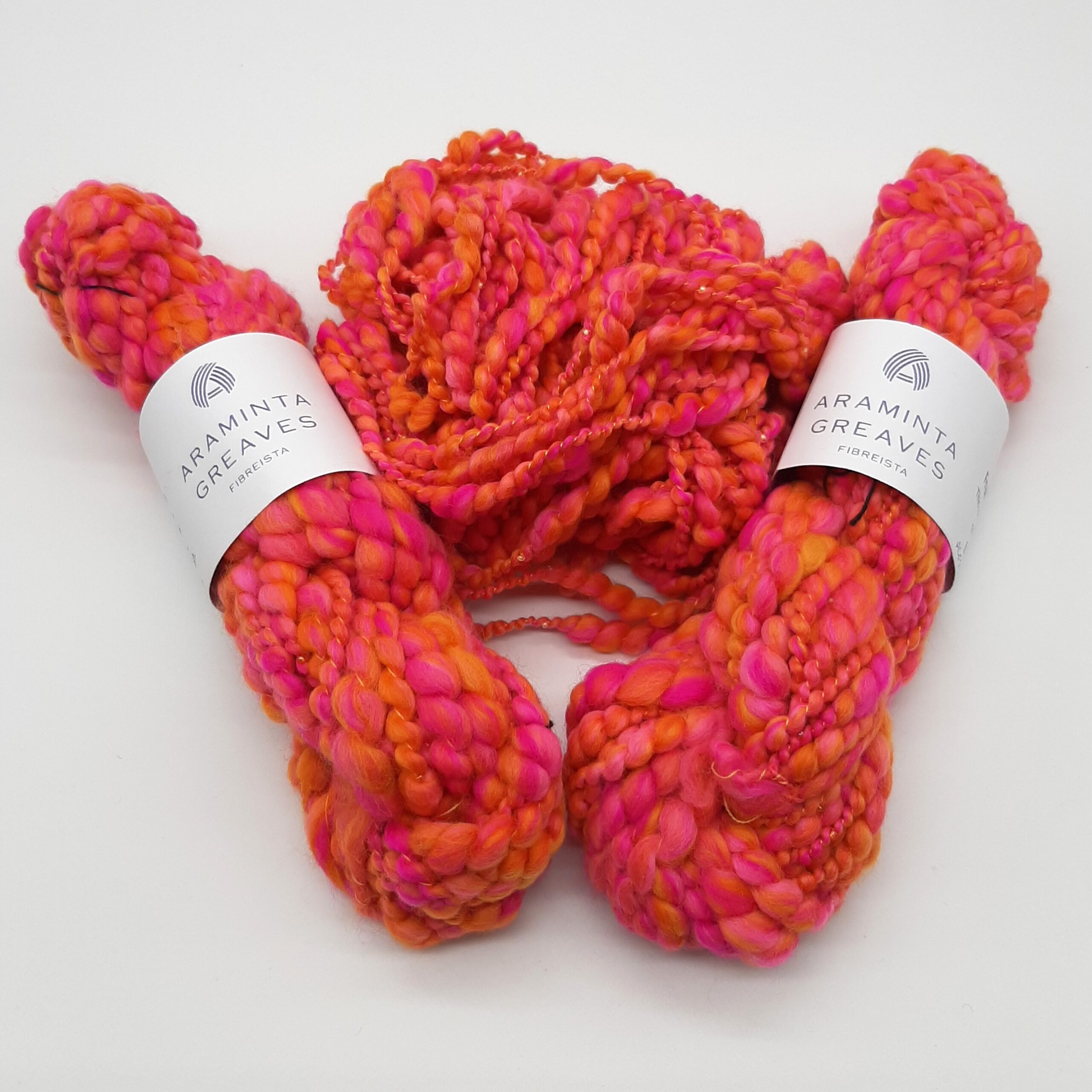 A ball and two skeins of Fruit Salads hand spun merino beaded yarn in vibrant shades of orange and pink.