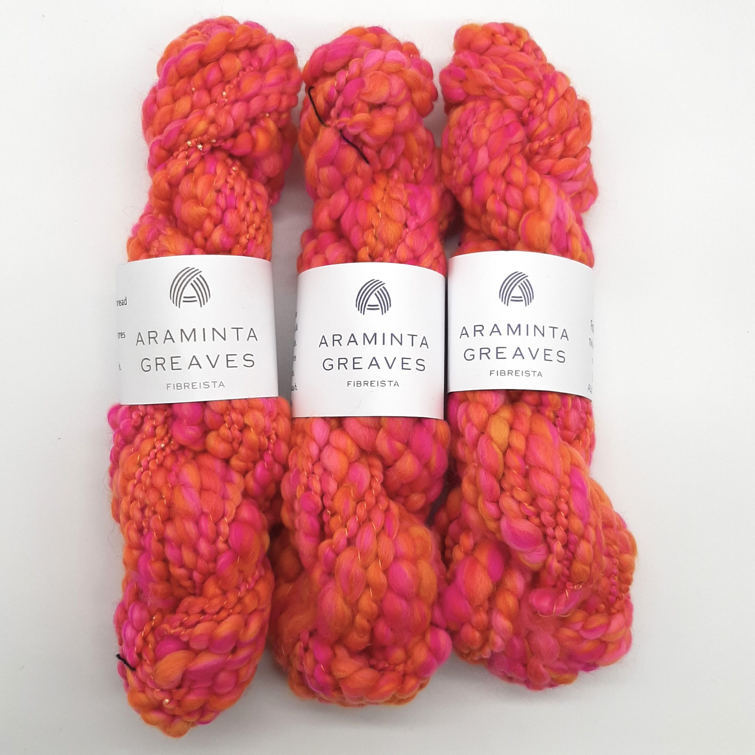 Three skeins of Fruit Salads hand spun merino beaded yarn in vibrant shades of orange and pink