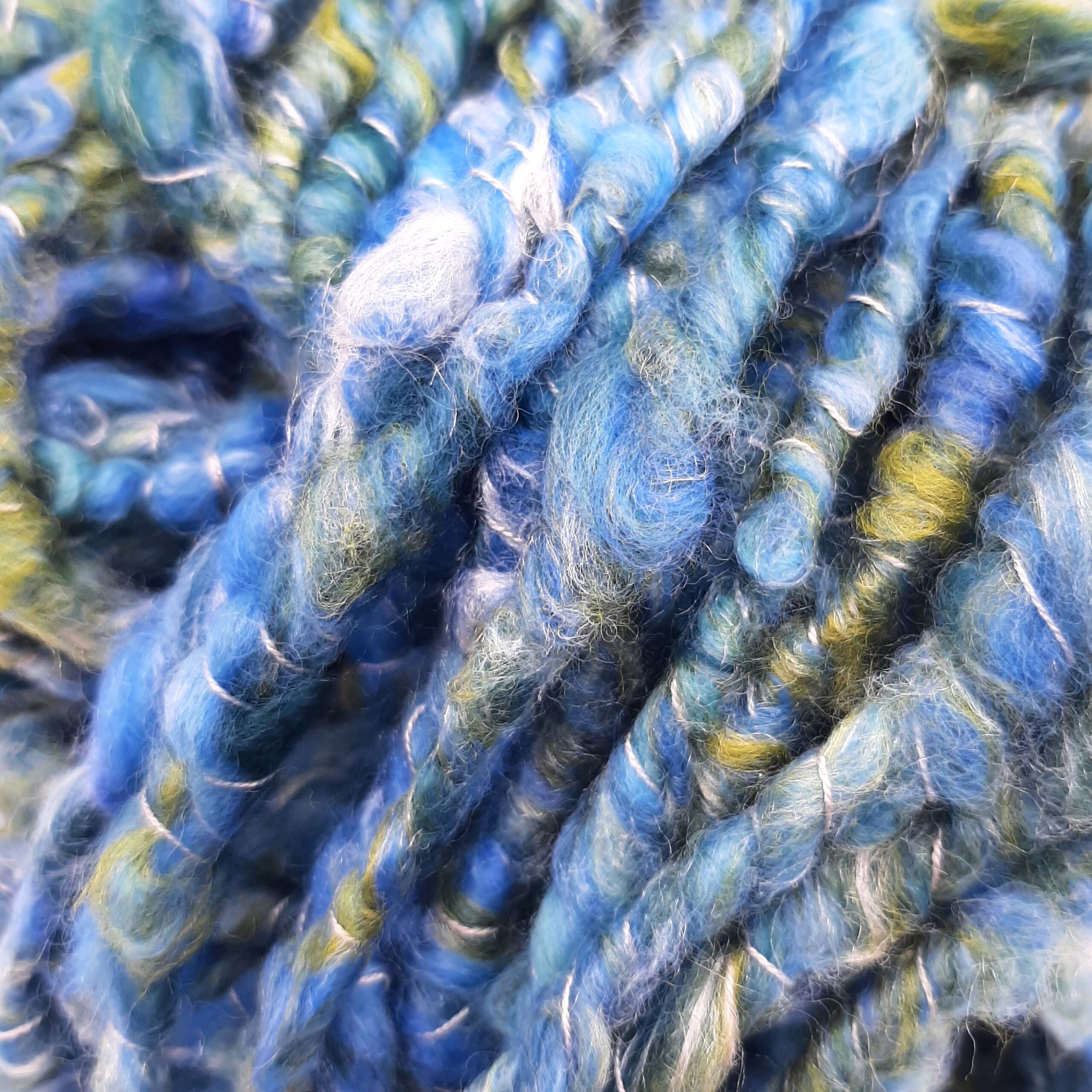A close up view of Polzeath Breeze handspun, corespun merino and silk yarn in blues and greens.