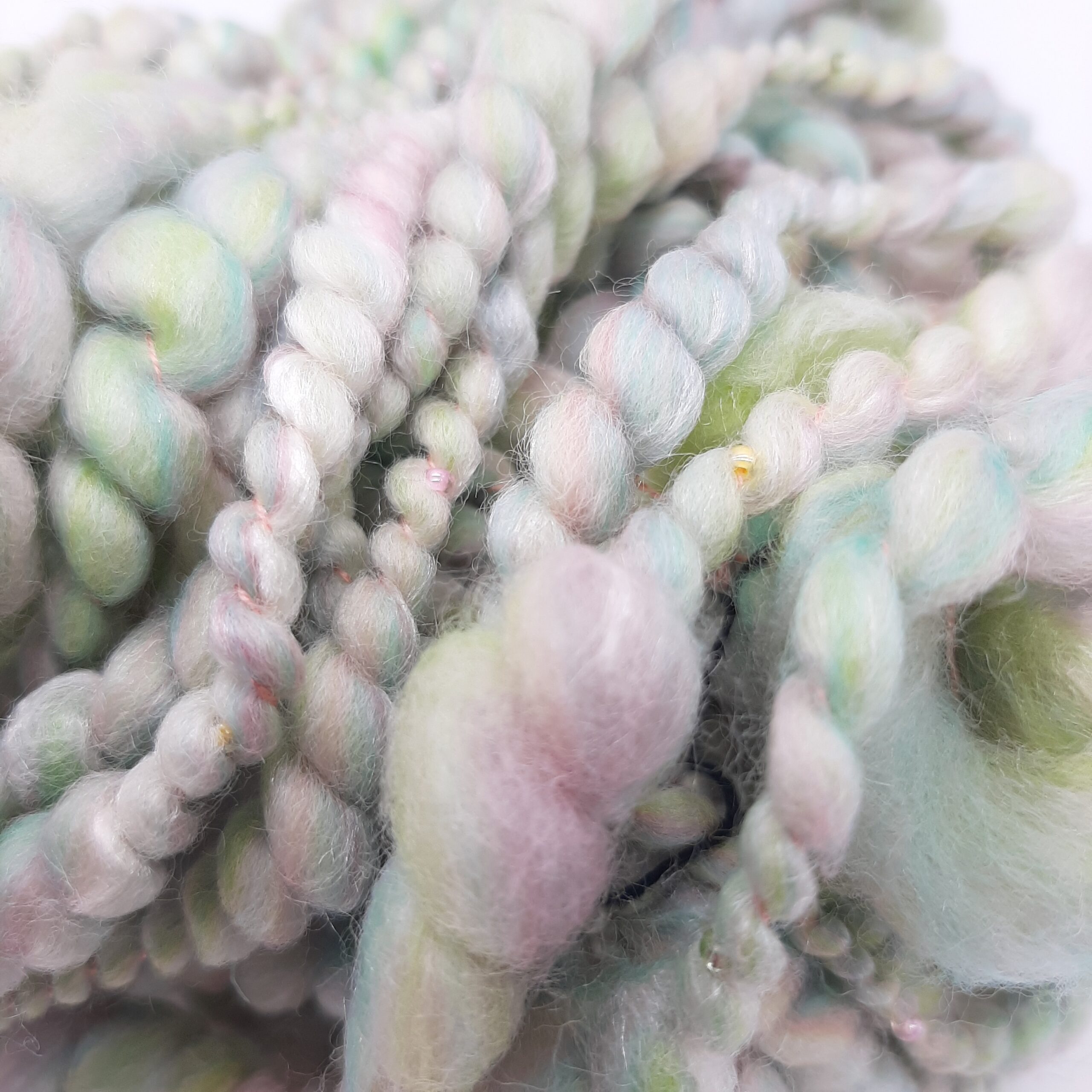A close up view of Sherbet Pips handspun, beaded yarn in pastel shades of greens and pinks.