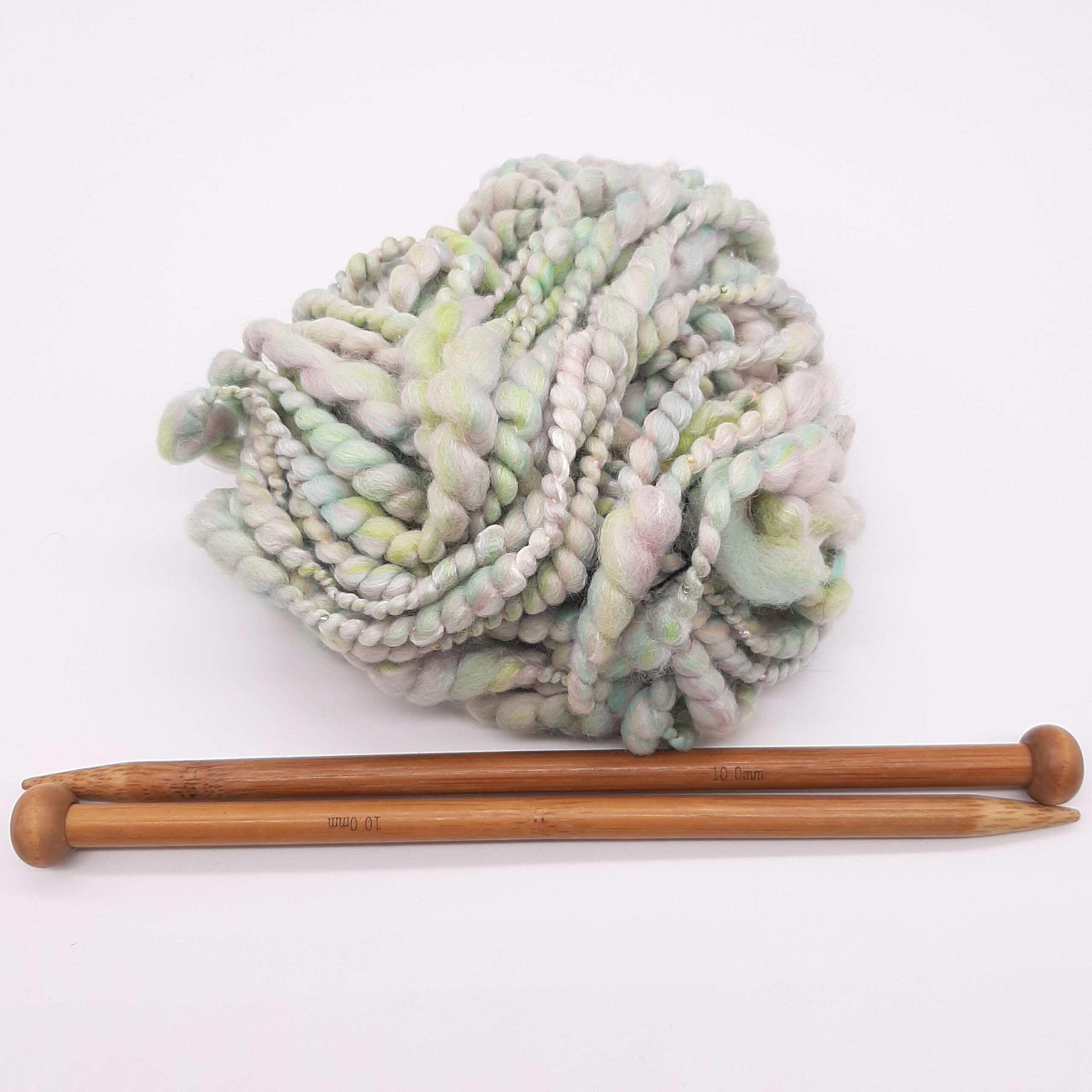 A ball of Sherbet Pips handspun, beaded yarn in pastel shades of greens and pinks, above a pair of bamboo knitting needles.