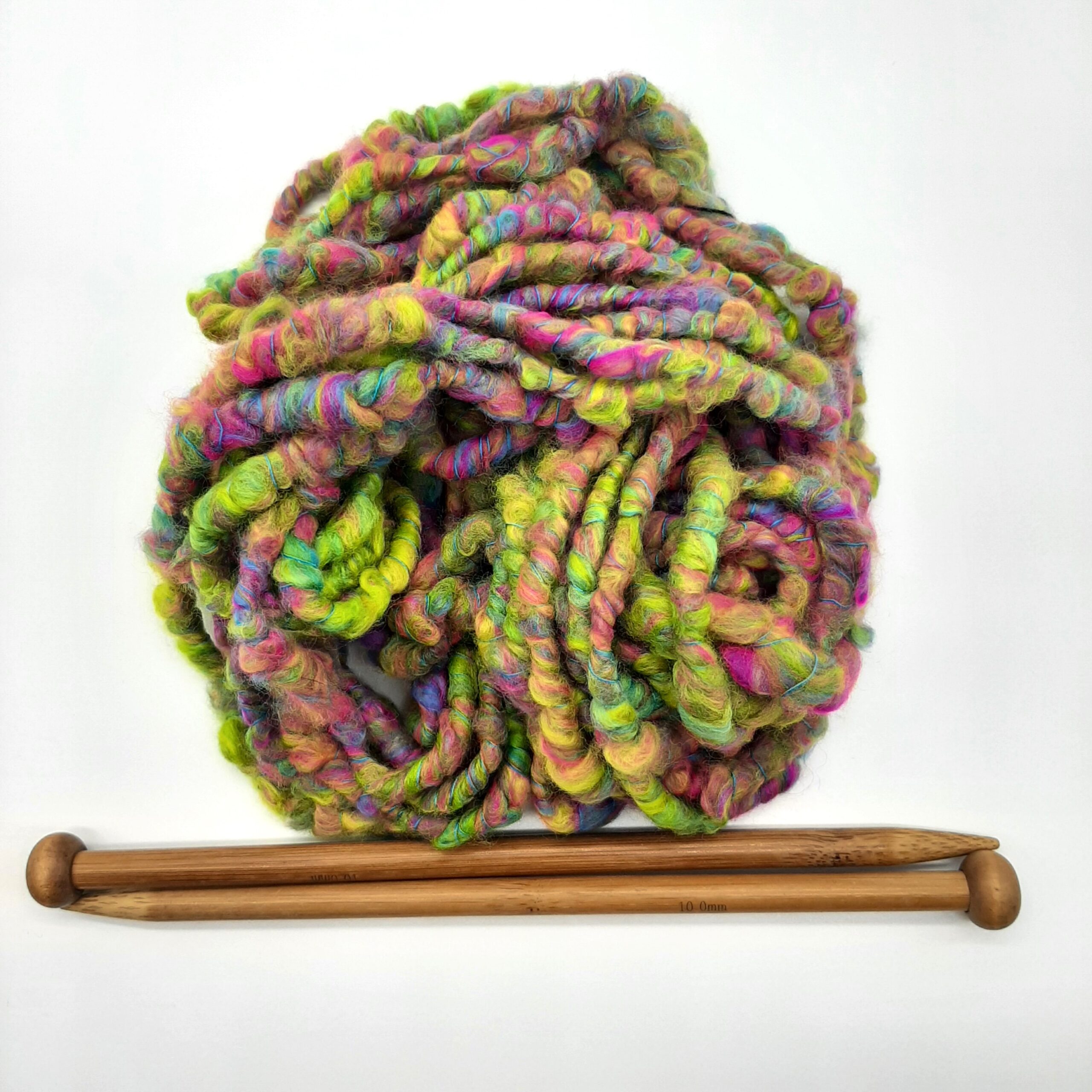 A ball of Summerleaze Beach Huts hand spun corespun merino yarn in vibrant yellow, pink, green and blue above a pair of bamboo needles.