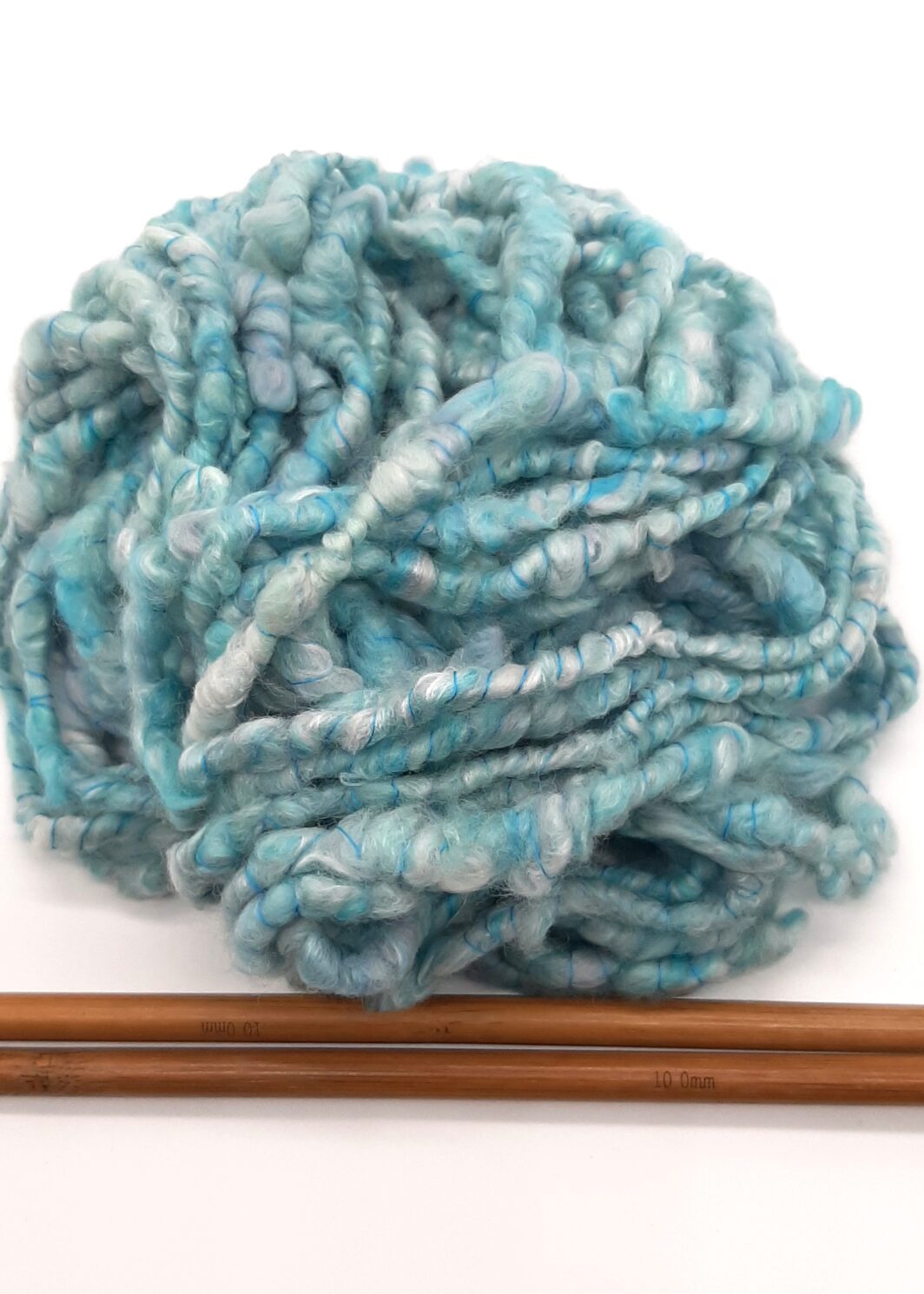 A ball of Trevone Foam, handspun corespun merion and silk yarn in pale blue, turquoise and grey above a pair of bamboo knitting needles.