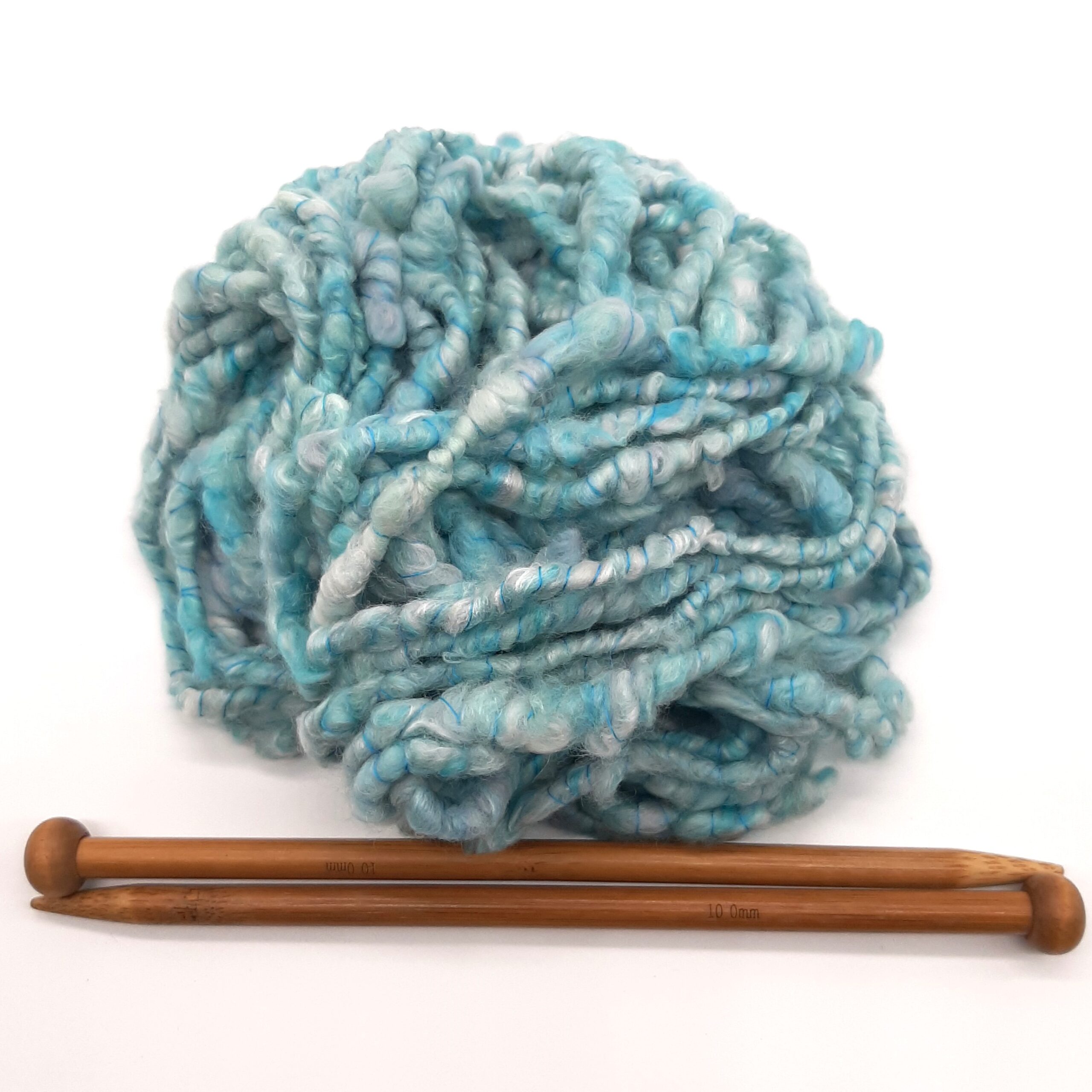 A ball of Trevone Foam, handspun corespun merion and silk yarn in pale blue, turquoise and grey above a pair of bamboo knitting needles.