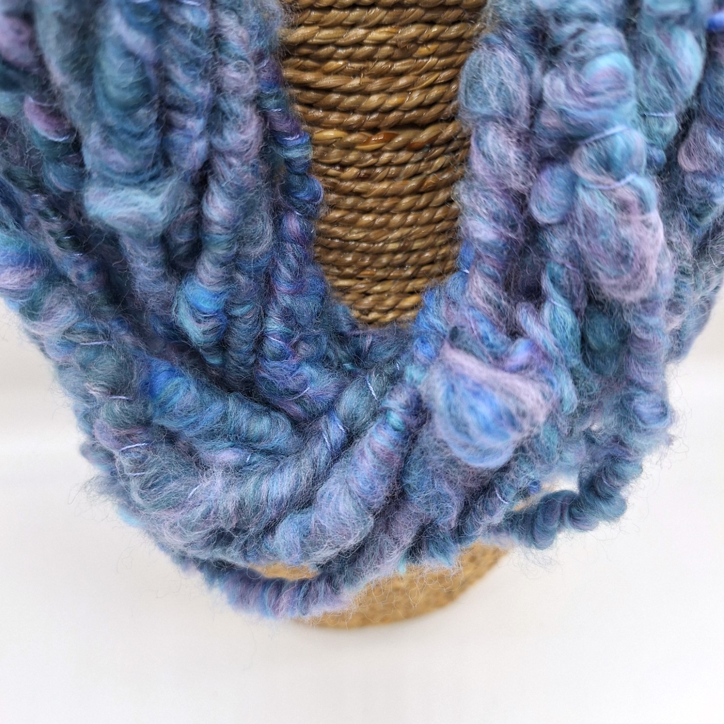 Close up of a hand spun merino cowl in shades of blue and mauve on a rattan bust.