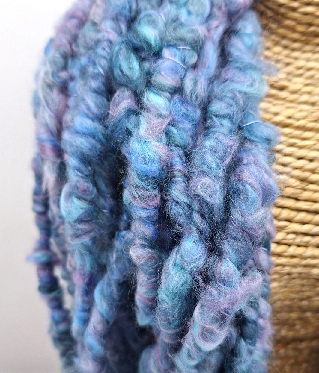 Close up of a hand spun merino cowl in shades of blue and mauve on a rattan bust.