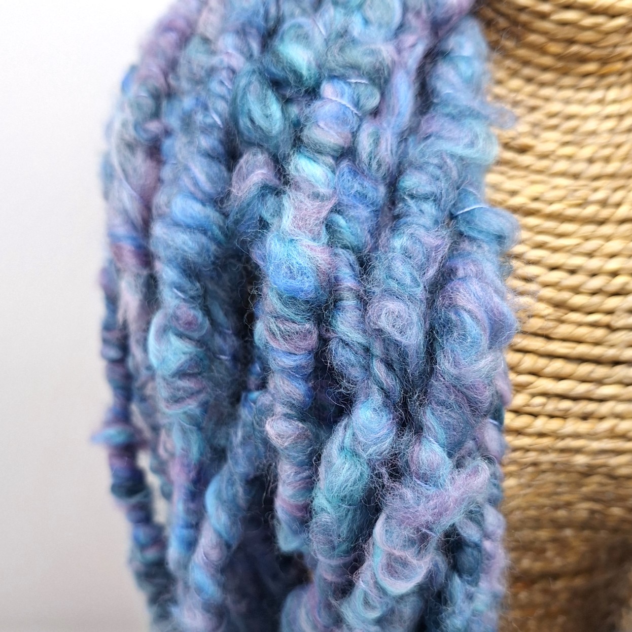 Close up of a hand spun merino cowl in shades of blue and mauve on a rattan bust.