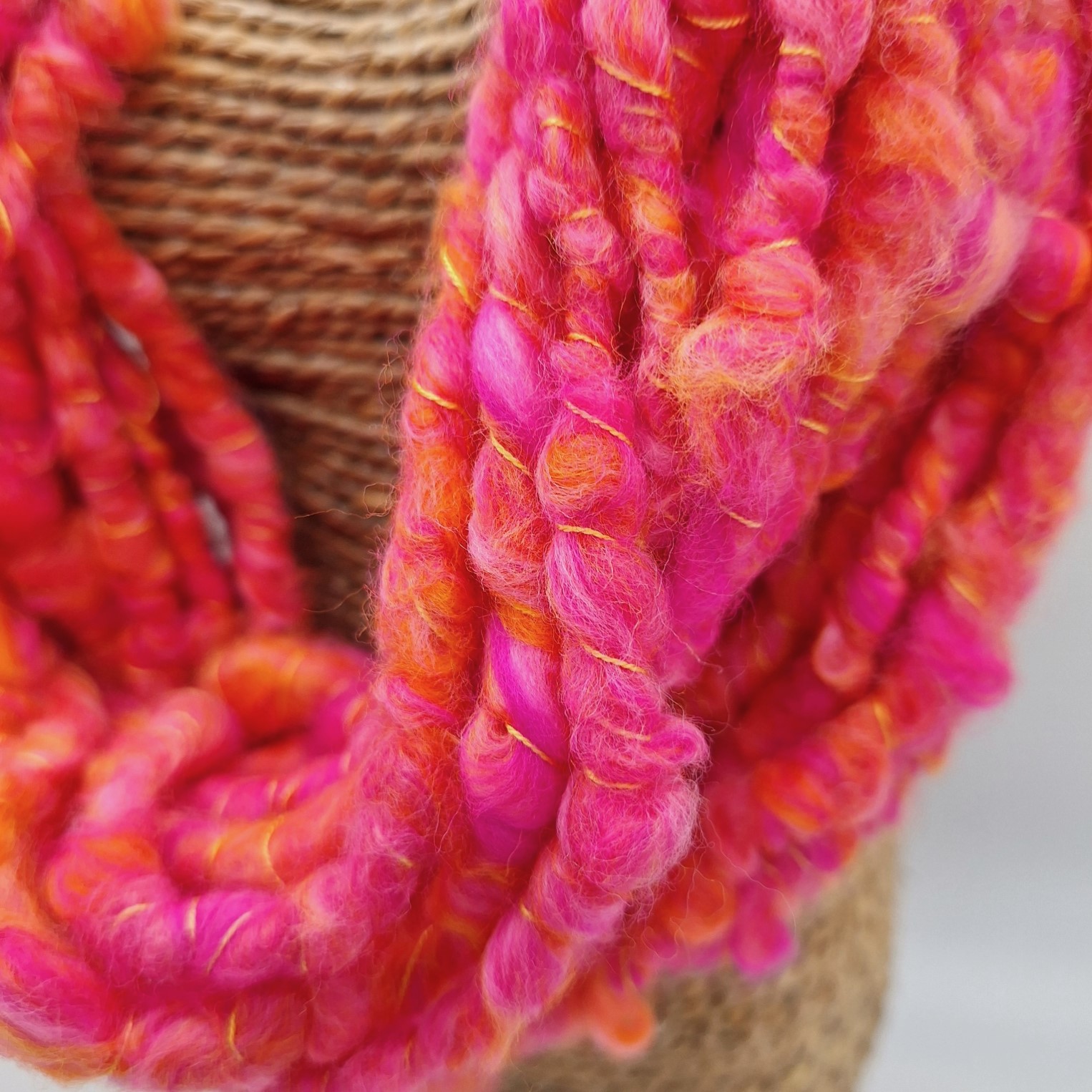 close up of a hand spun cowl neckwarmer in shades of orange and pink merino wool on a rattan bust