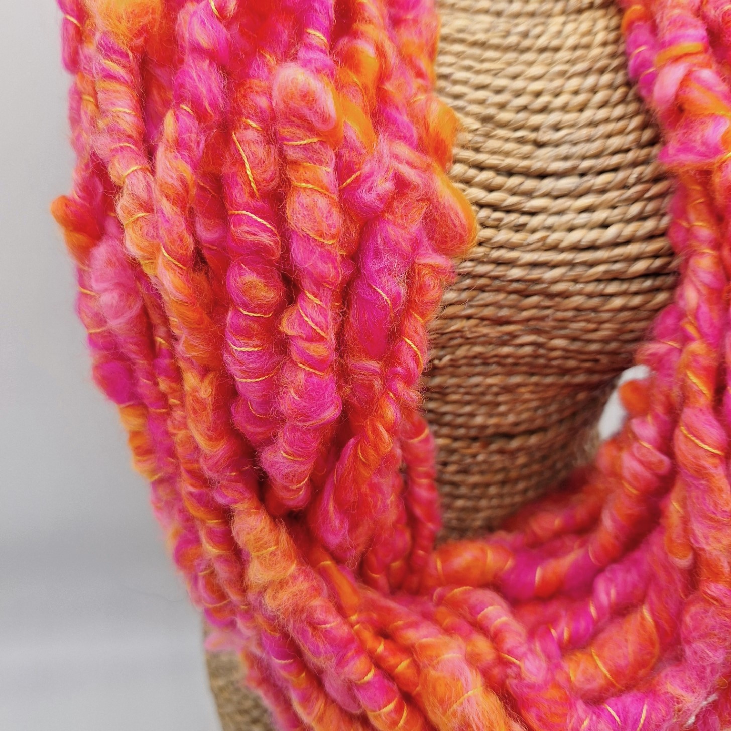 close up of a hand spun cowl neckwarmer in shades of orange and pink merino wool on a rattan bust