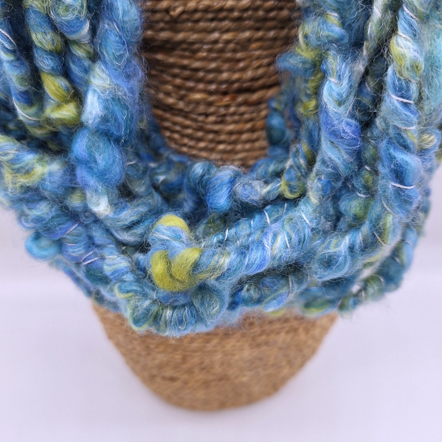 Close up of a merino and silk hand spun cowl neckwarmer in shades of blue and green on a rattan bust