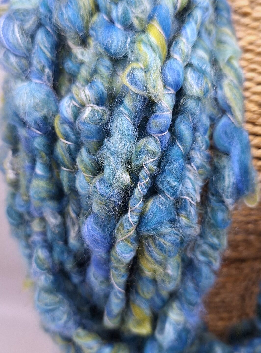 Close up of a merino and silk hand spun cowl neckwarmer in shades of blue and green on a rattan bust.