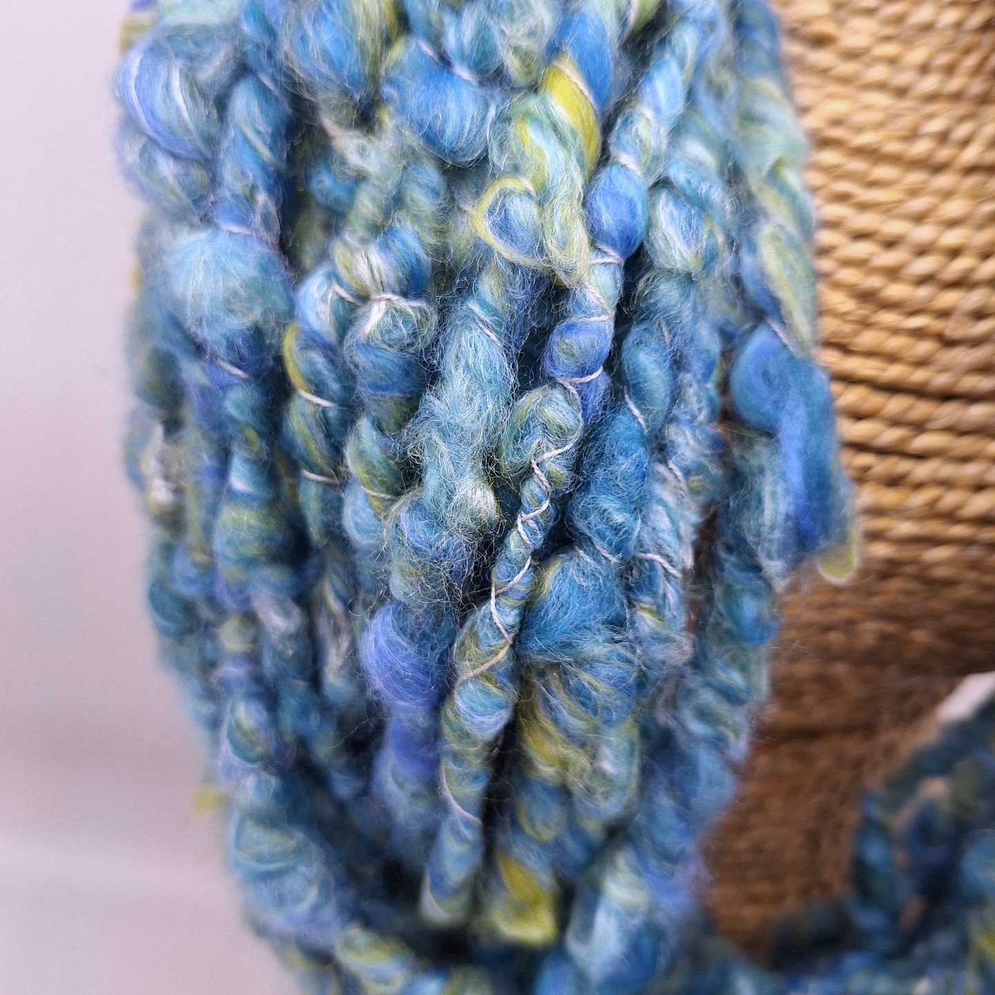 Close up of a merino and silk hand spun cowl neckwarmer in shades of blue and green on a rattan bust.