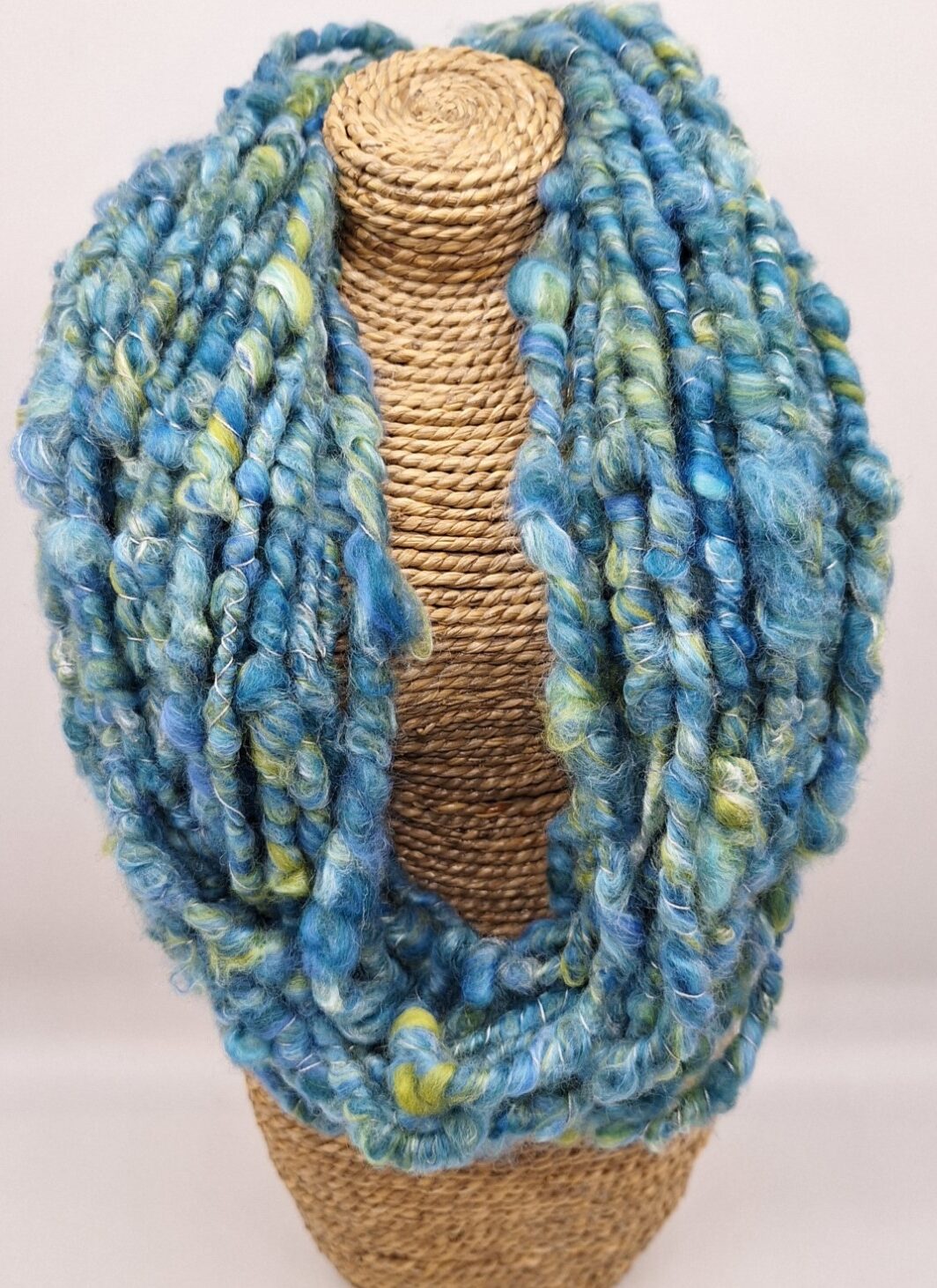 Hand spun merino and silk cowl in shades of blue and green on a rattan bust.