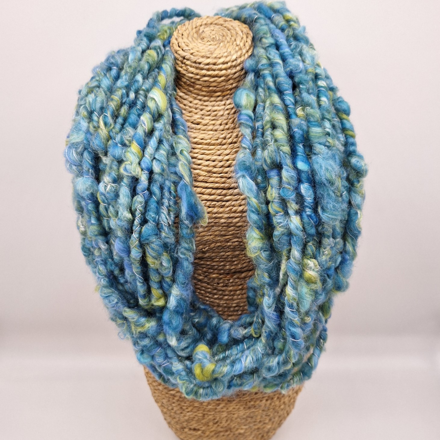 Hand spun merino and silk cowl in shades of blue and green on a rattan bust.