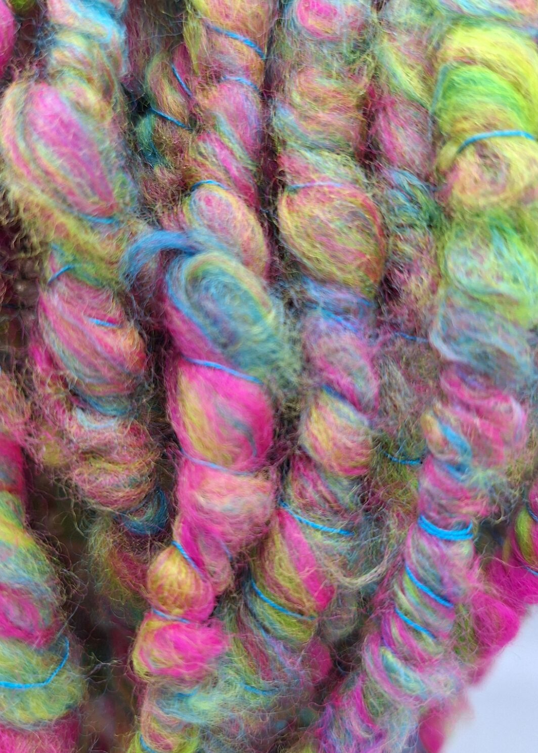 Close up of a merino hand spun cowl in vibrant shades of pink, blue, lime green and yellow, plied with a turquoise Italian silk thread.