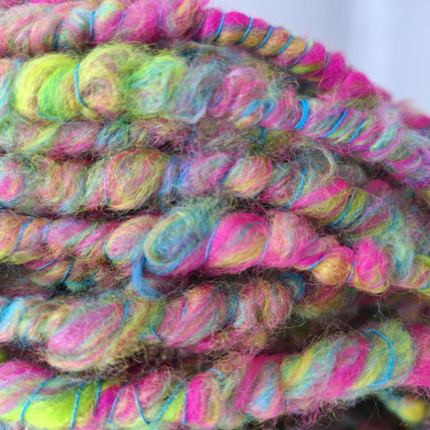 Close up of a merino hand spun cowl in vibrant shades of pink, blue, lime green and yellow, plied with a turquoise Italian silk thread.
