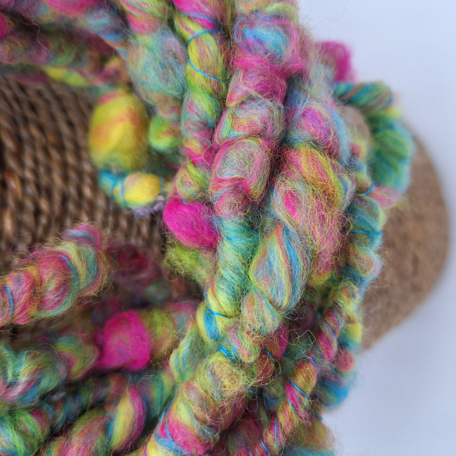 Close up of a merino hand spun cowl in vibrant shades of pink, blue, lime green and yellow, plied with a turquoise Italian silk thread.