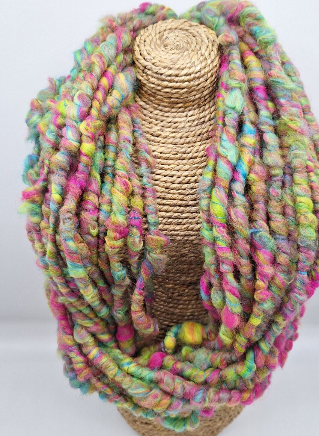 Hand spun merino cowl in vibrant pink, blue, lime green and yellow on a rattan bust.