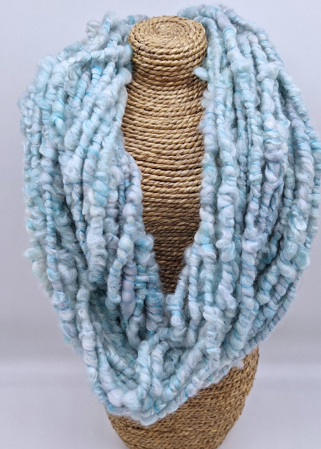 Hand spun merino and silk cowl in shades of pale blues and greys on a rattan bust.