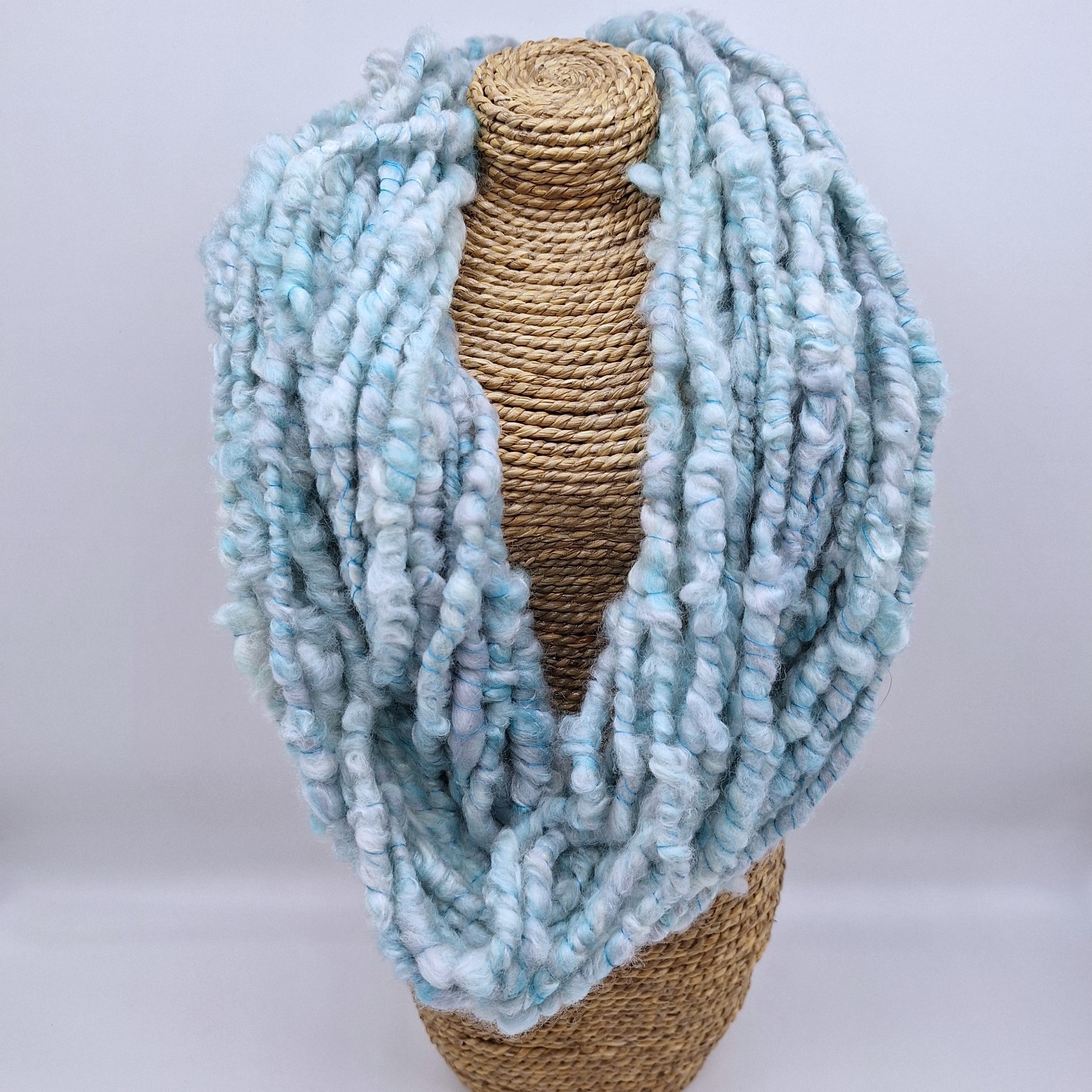 Hand spun merino and silk cowl in shades of pale blues and greys on a rattan bust.