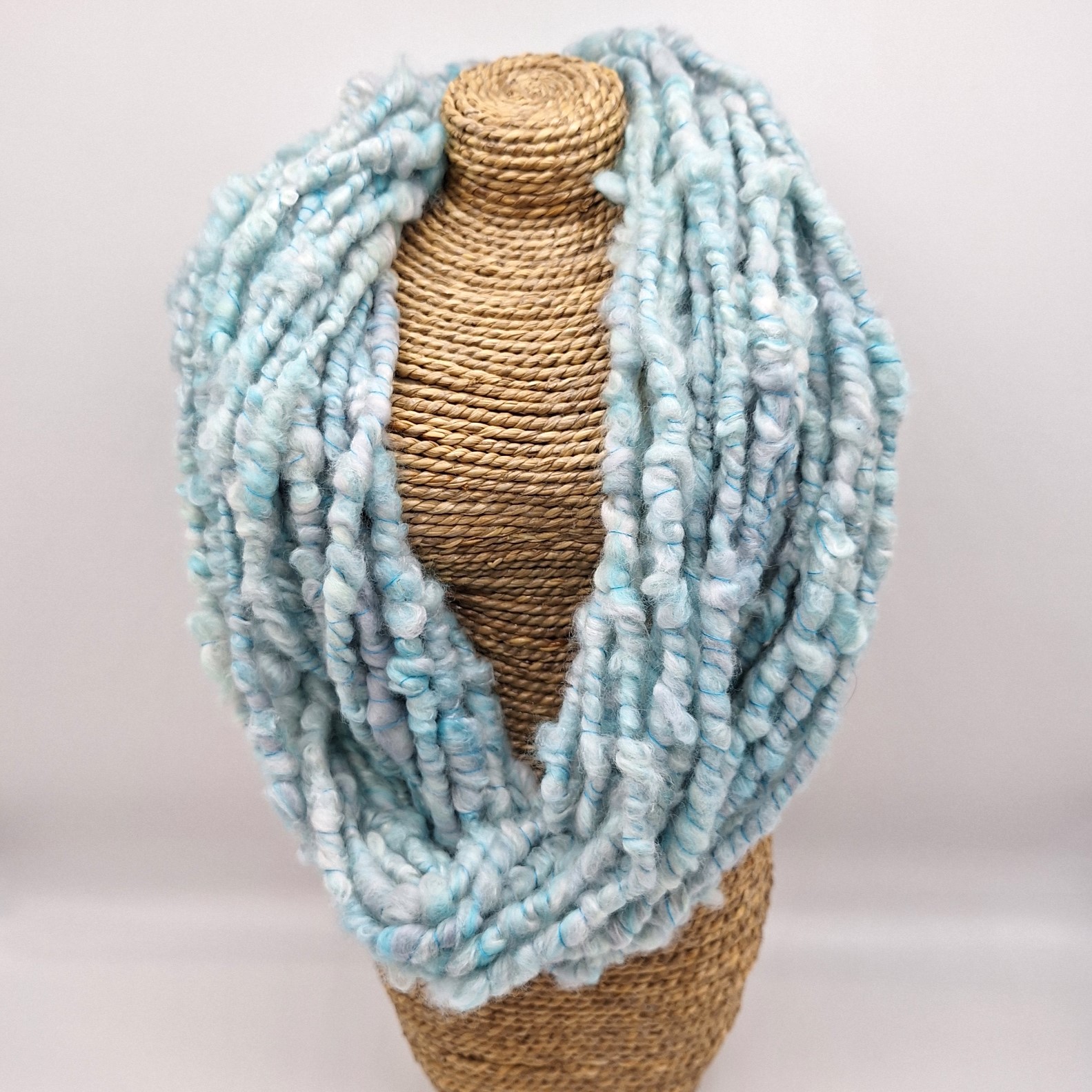 Hand spun merino and silk cowl in shades of pale blues and greys on a rattan bust.