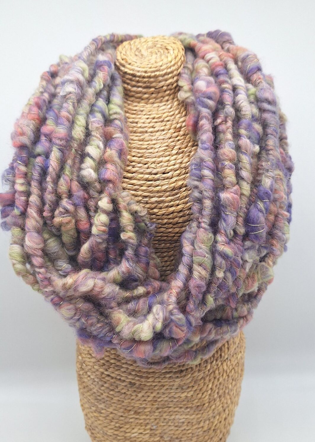 Hand spun merino wool cowl neckwarmer in muted shades of purple, green and pink on a display bust