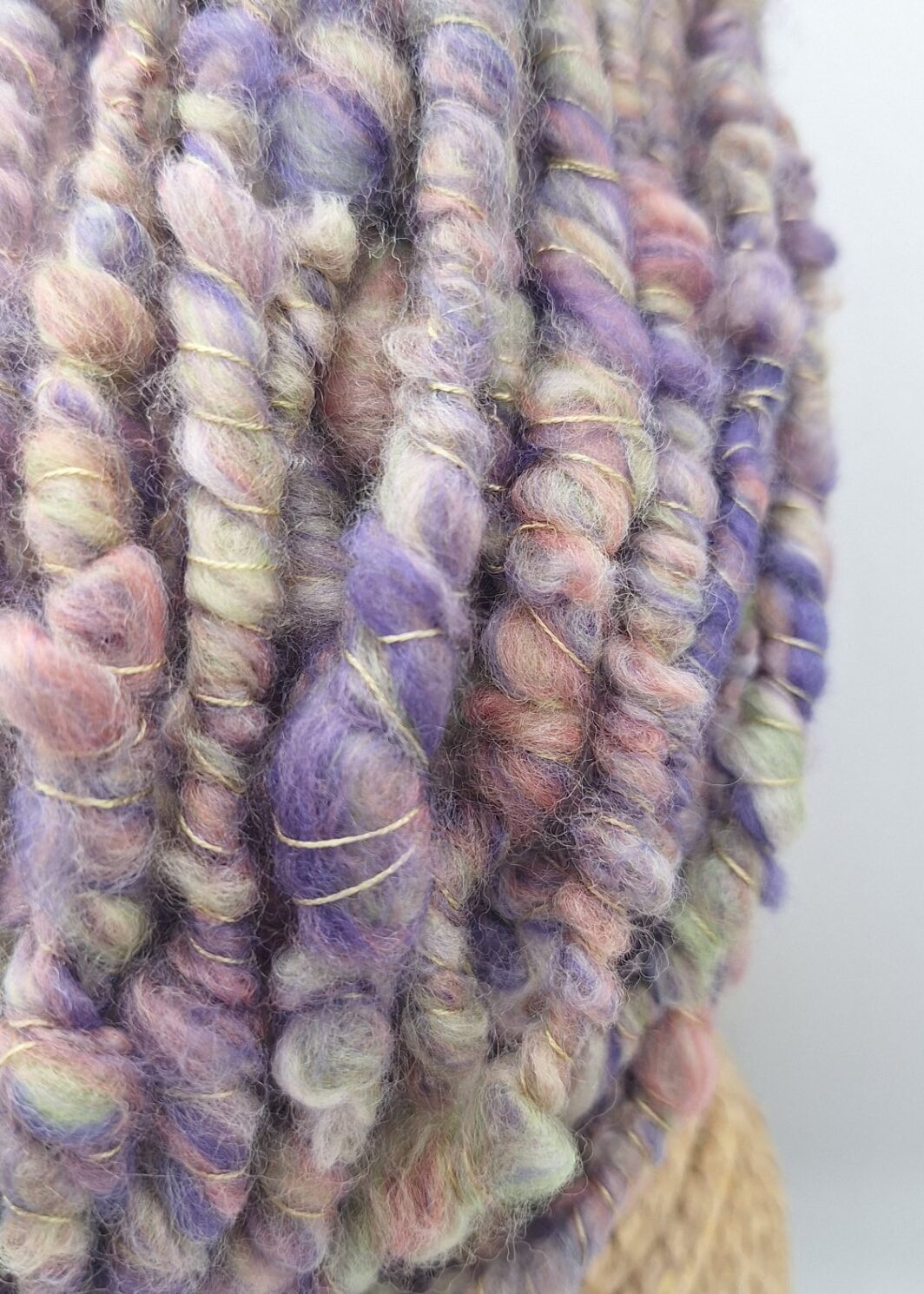 close up view of a hand spun merino wool cowl neckwarmer in muted shades of purple, green and pink