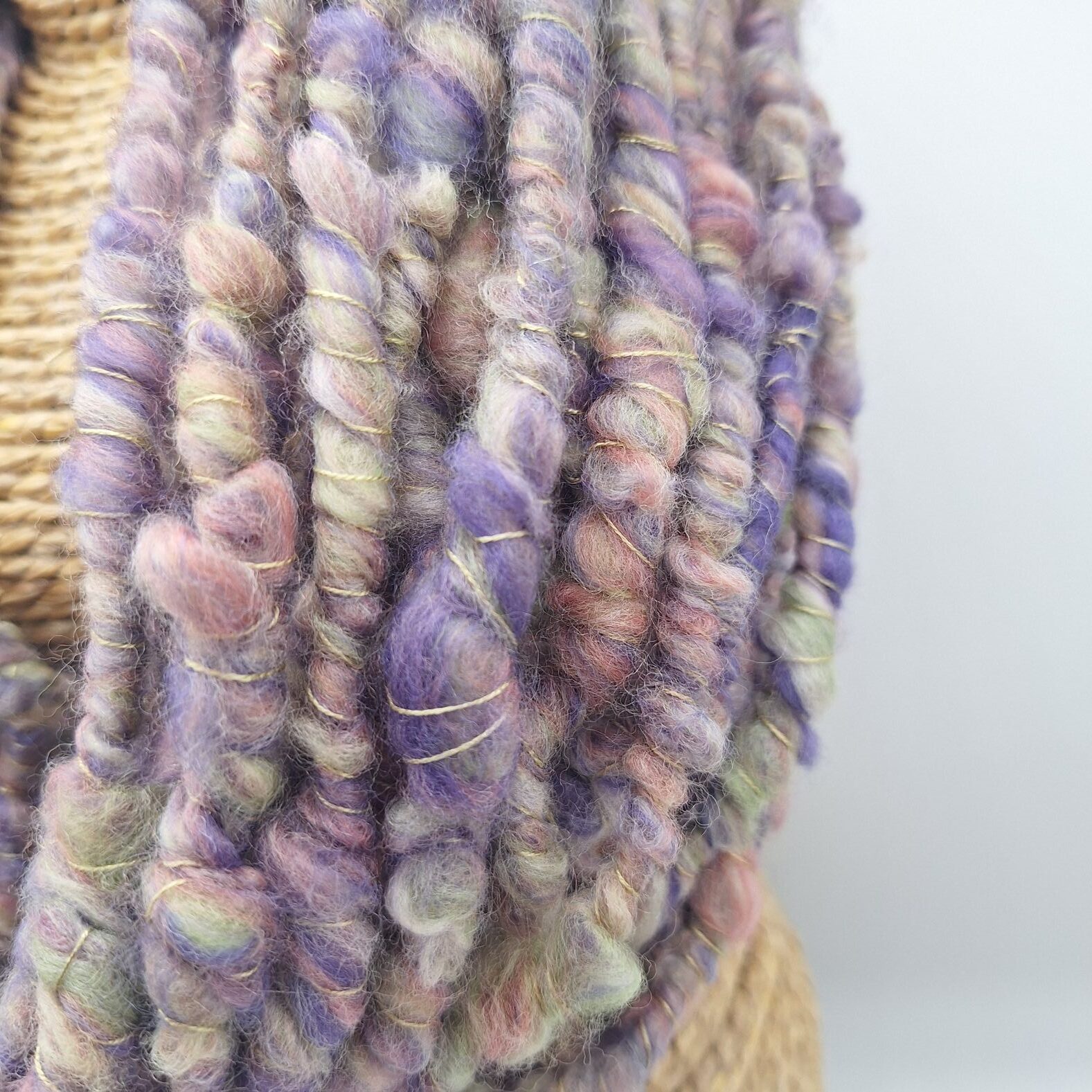 close up view of a hand spun merino wool cowl neckwarmer in muted shades of purple, green and pink