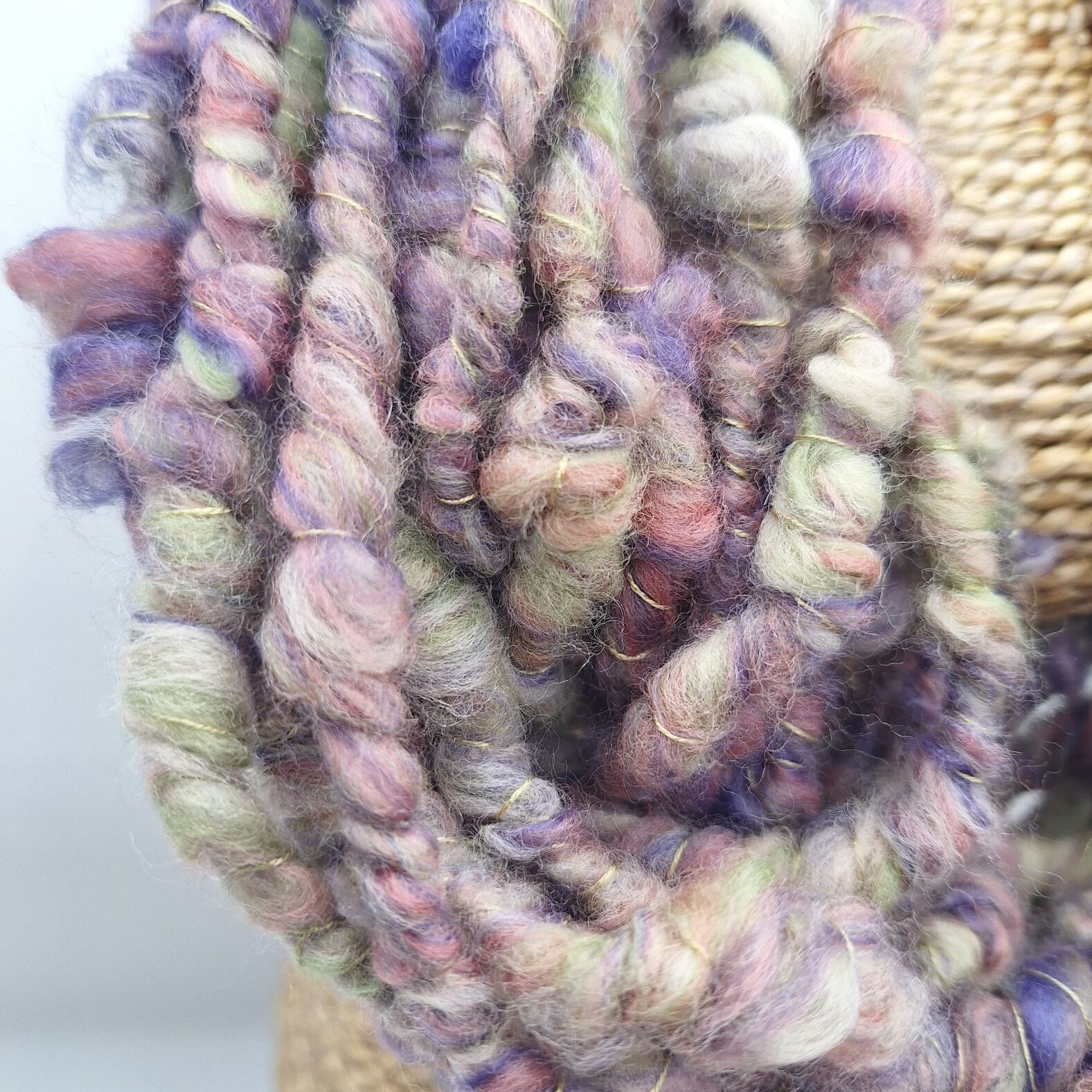 Close up view of hand spun merino wool cowl in muted shades of purple, green and pink