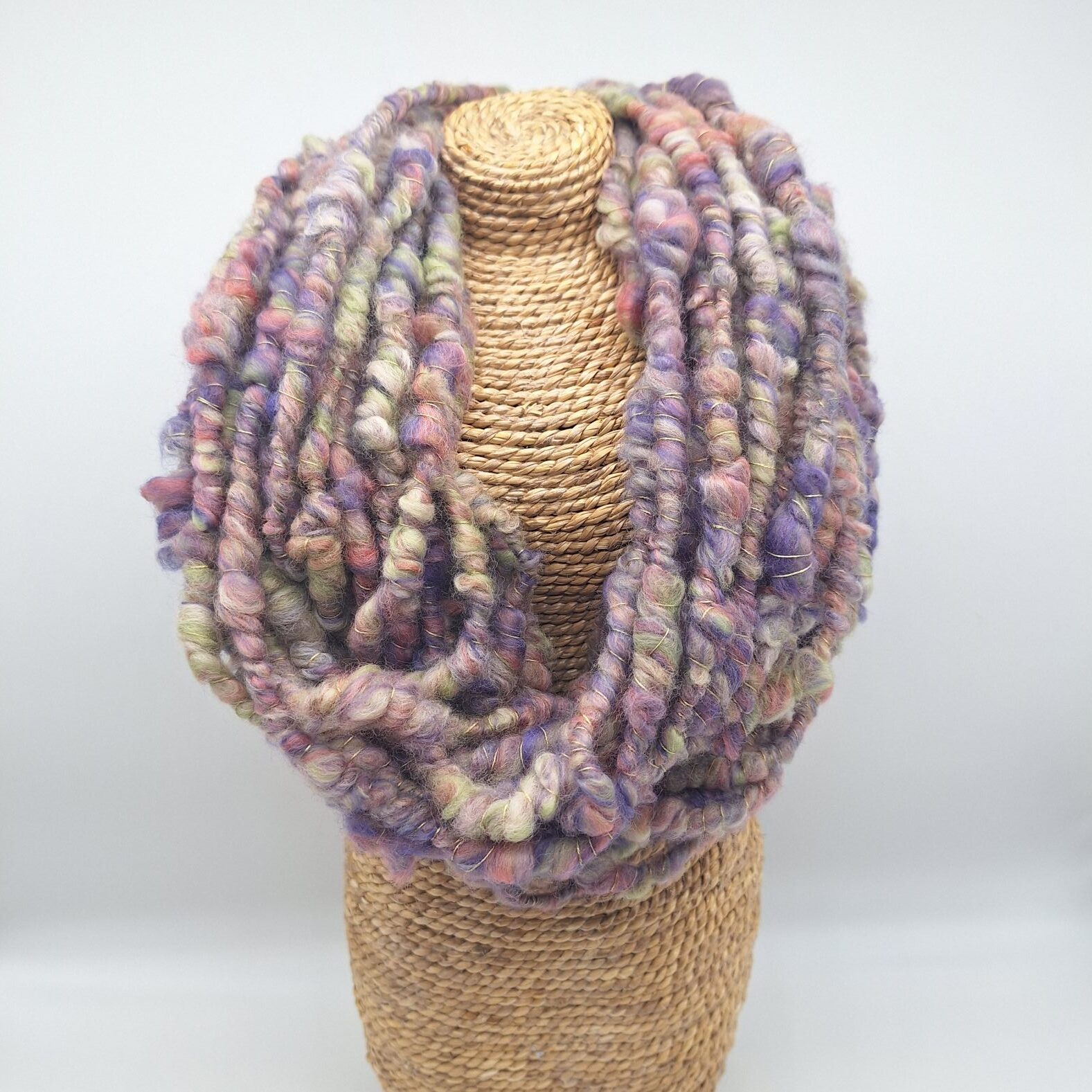 Hand spun merino wool cowl neckwarmer in muted shades of purple, green and pink on a display bust