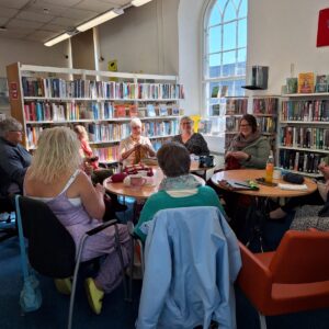 Group of women knitting and crocheting, sitting around round tables in Camelford Library