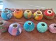Colourful spherical felt vessels in two rows on a brown towel.